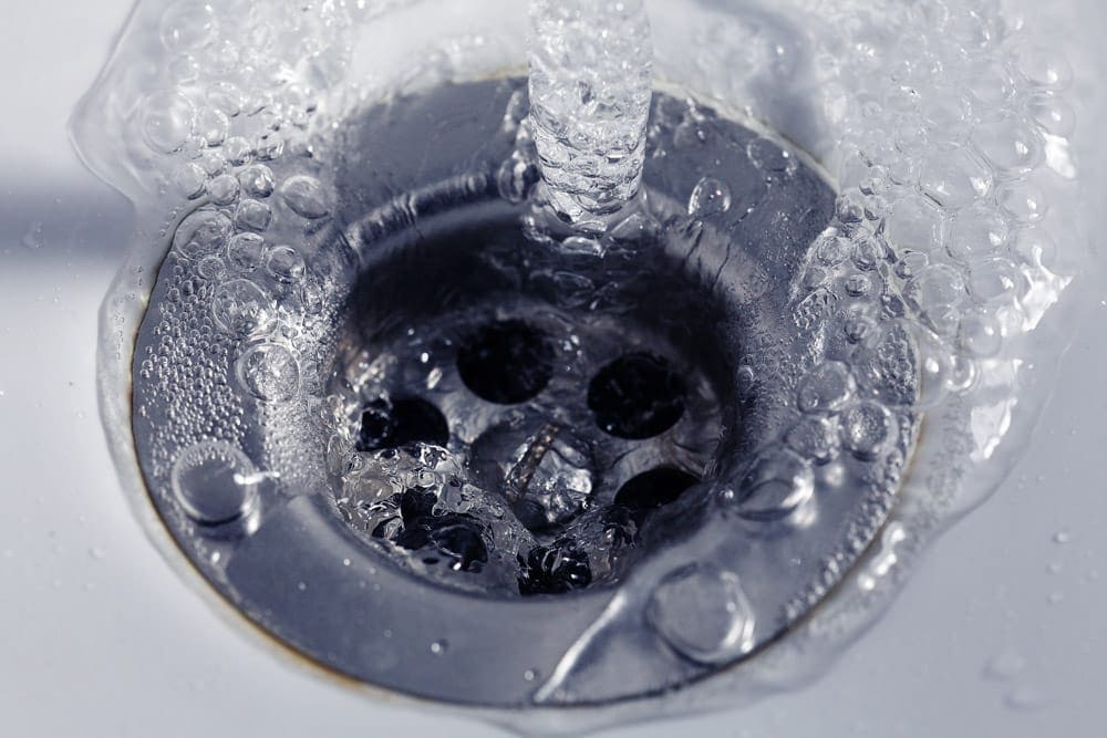 Running water flows into a metal sink drain, surrounded by bubbles.