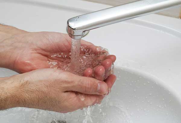 Hands cupped under a running faucet collecting water in a sink.