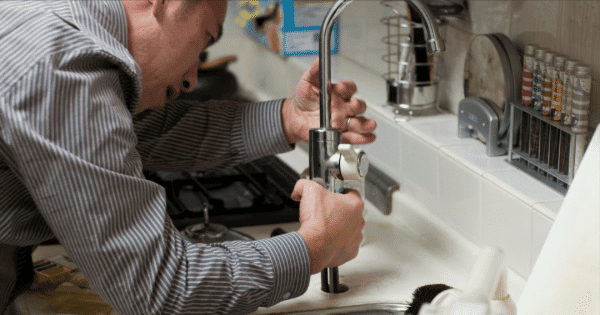 Person repairing a kitchen faucet, focusing on tightening the tap.