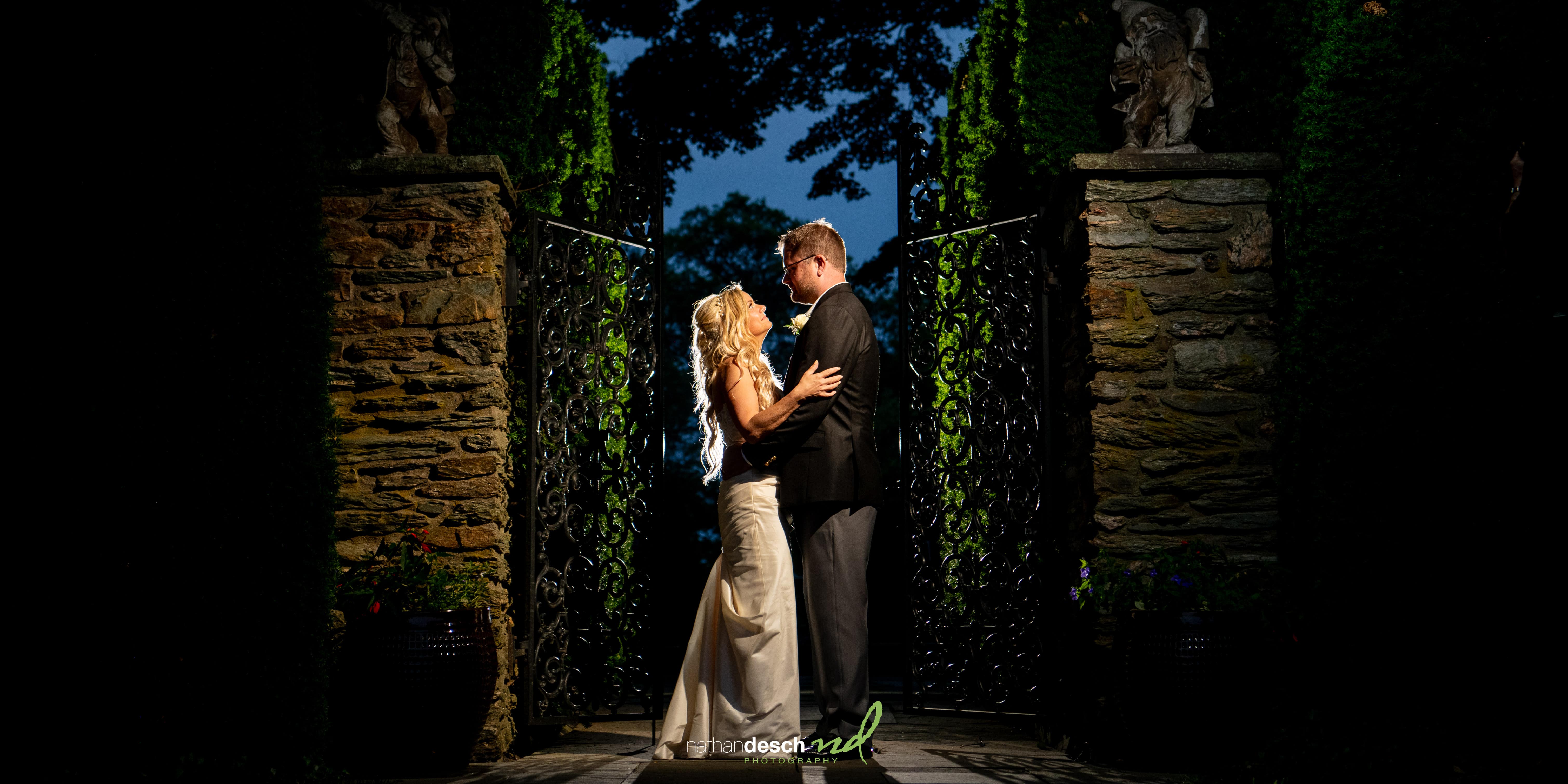 Bride and groom at night, softly lit at Drumore Estate with stone walls, iron gates, and lush greenery in the background.