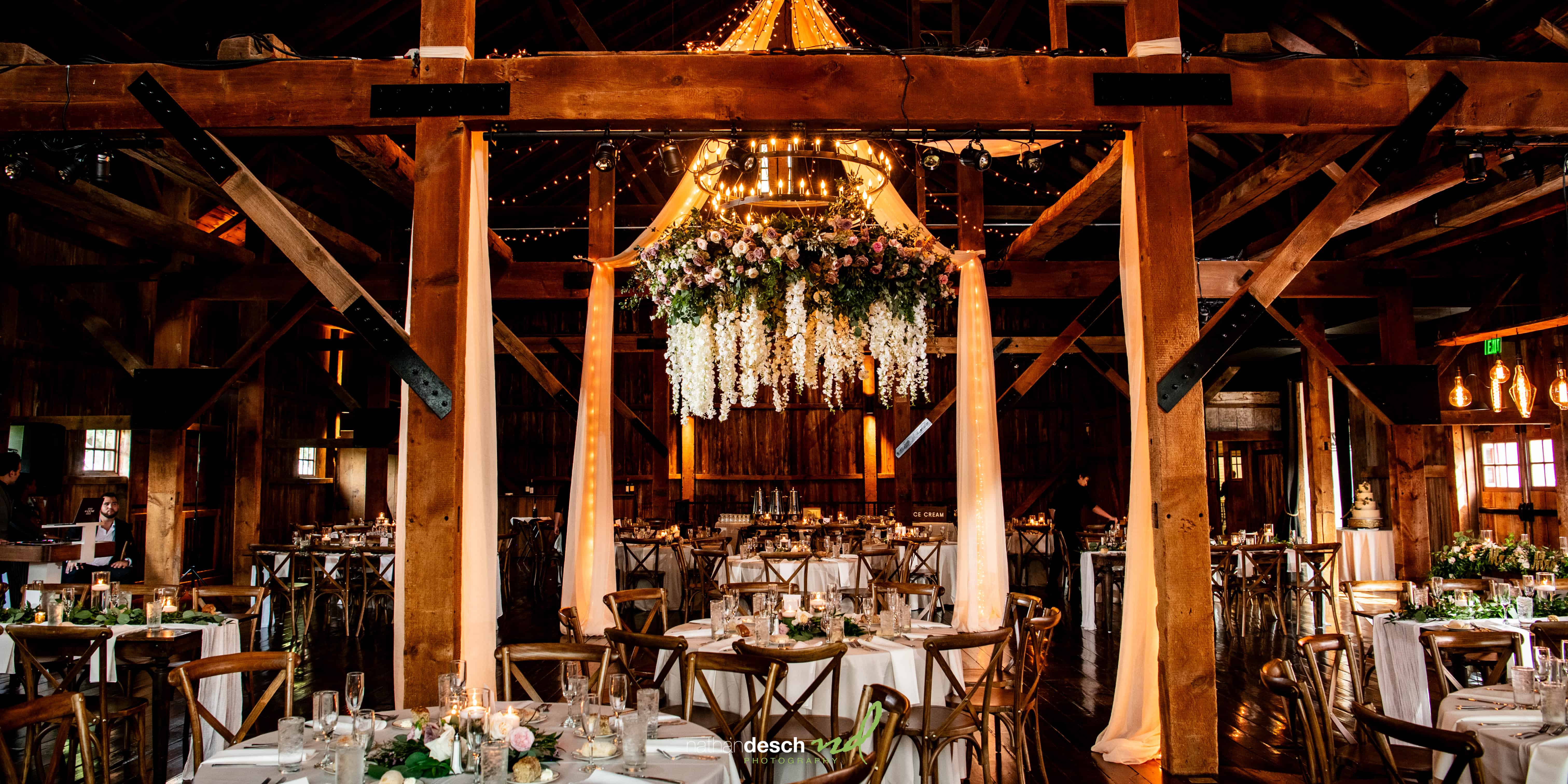 Rustic summer wedding reception at Farm at Eagles Ridge barn, round tables, white linens, floral centerpieces, chandelier.