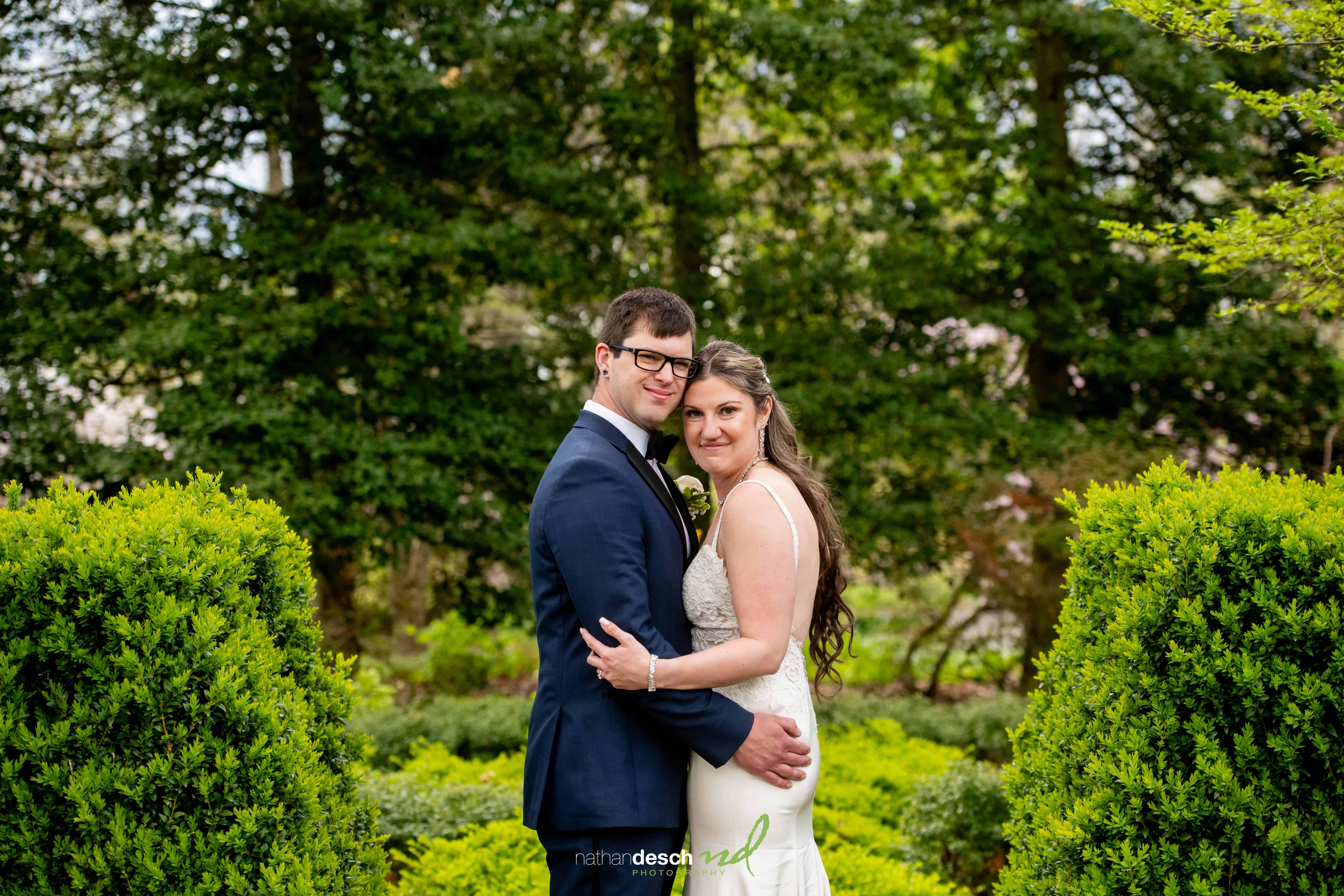 Bride and groom smiling together in a lush outdoor garden with greenery, captured by wedding photographer.
