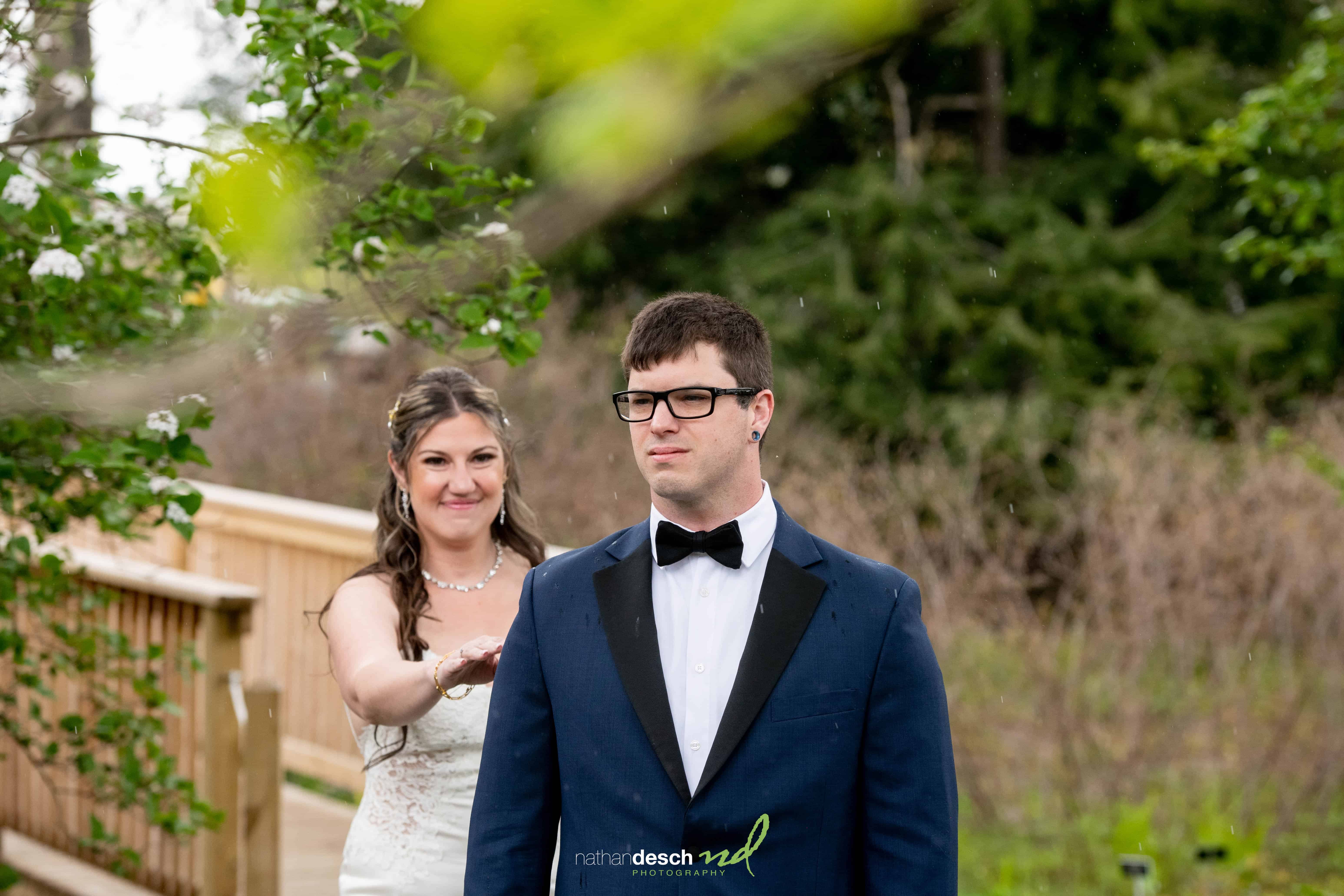 Bride in white smiling as she meets groom in navy suit for first look on wooden bridge at Frelinghuysen Arboretum wedding.