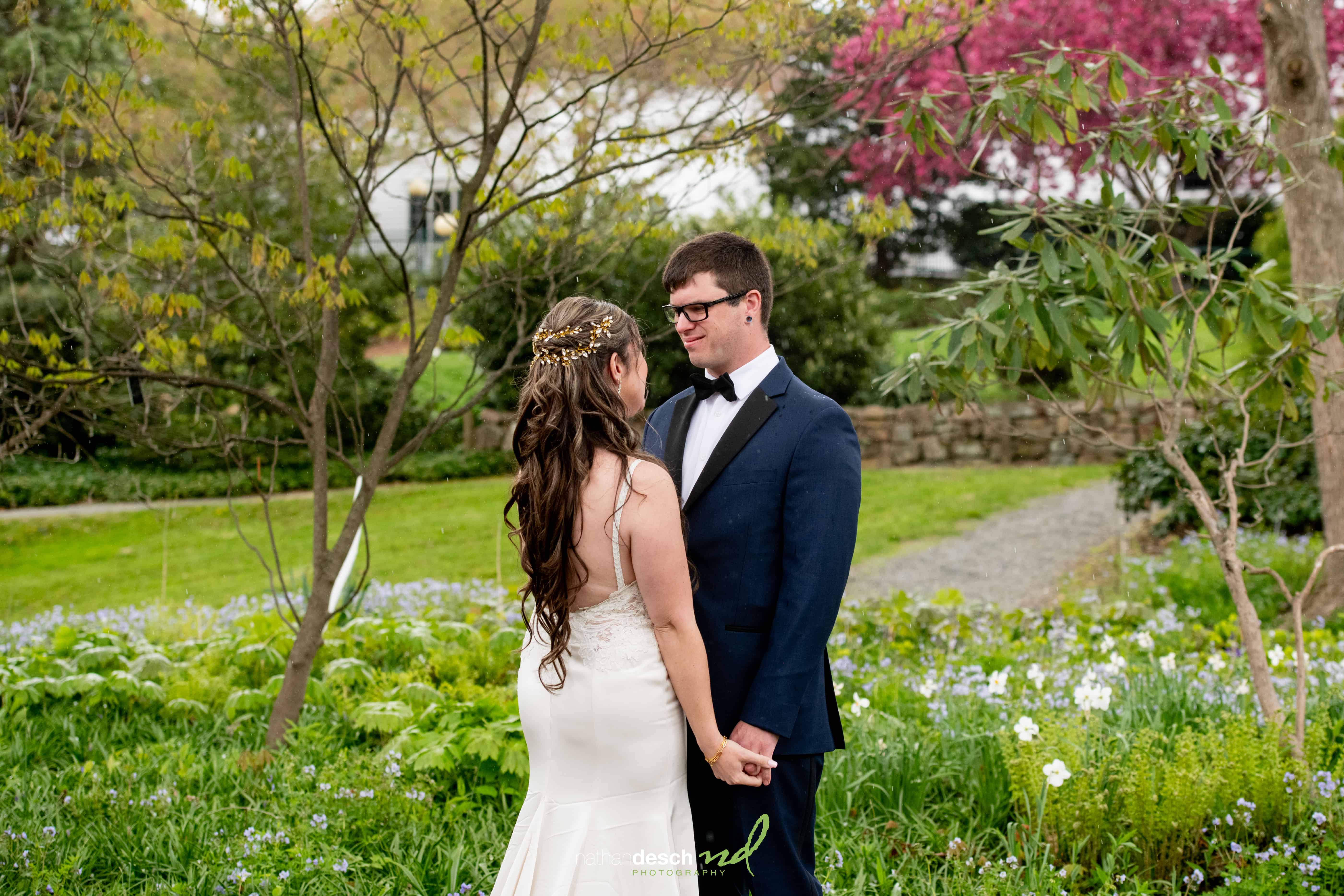 Bride and groom holding hands in lush Frelinghuysen Arboretum garden wedding, surrounded by greenery and blooming flowers.