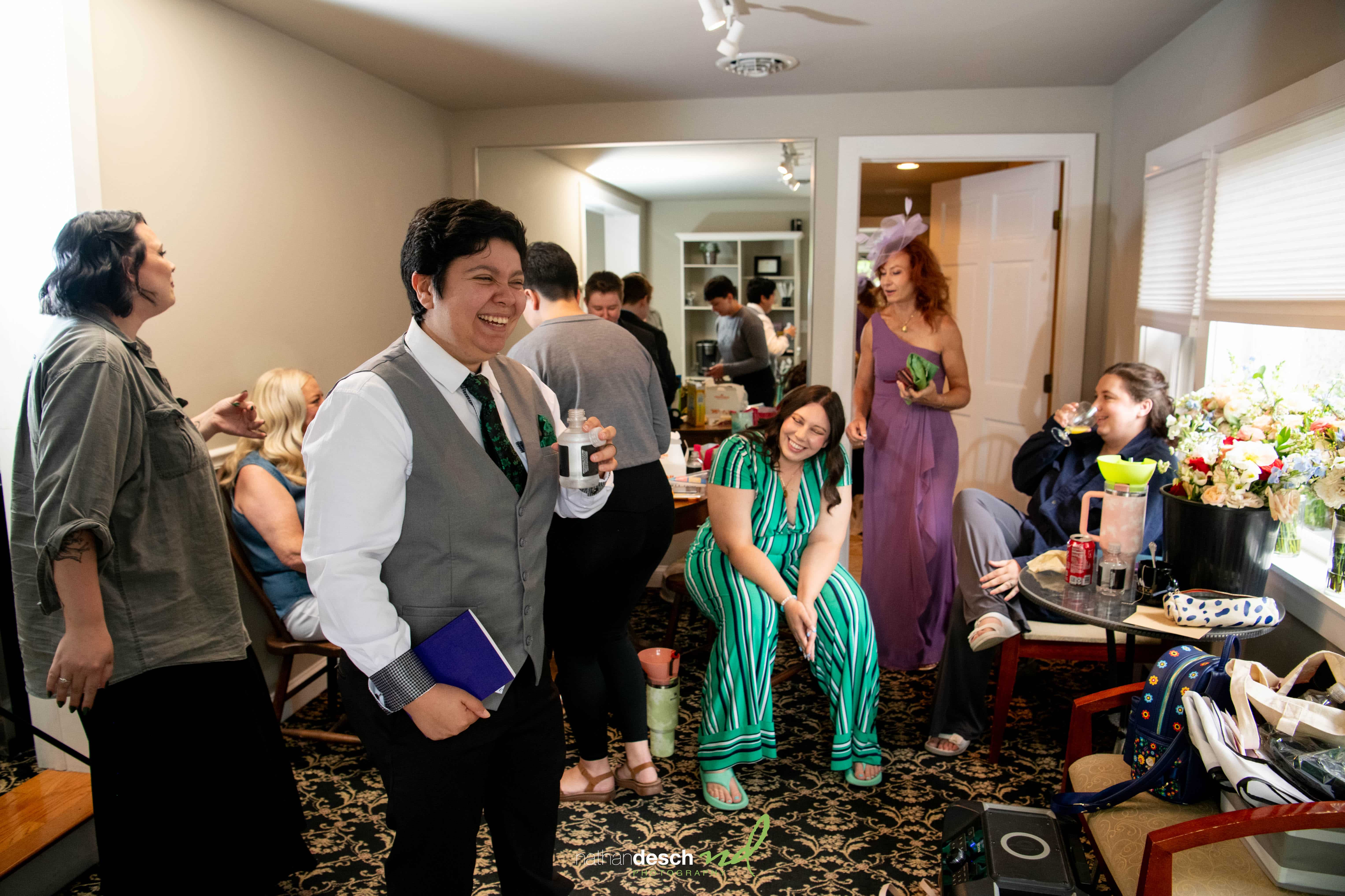 Jake and Erika laughing with friends in a cozy, well-lit room during a joyful, semi-formal wedding celebration.
