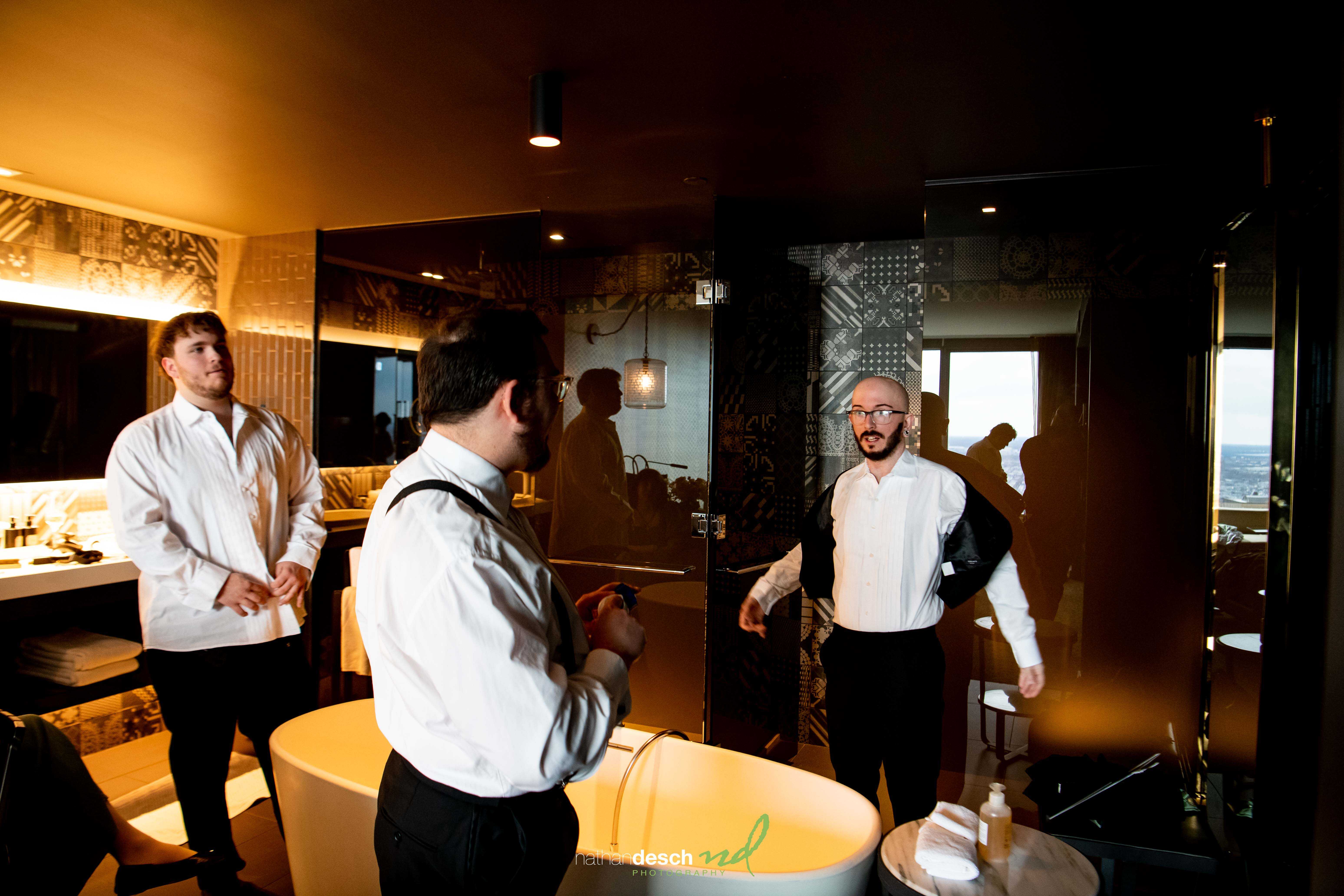 Groomsmen getting ready in a modern bathroom at Tendenza wedding, two in white shirts, relaxed and candid moment.