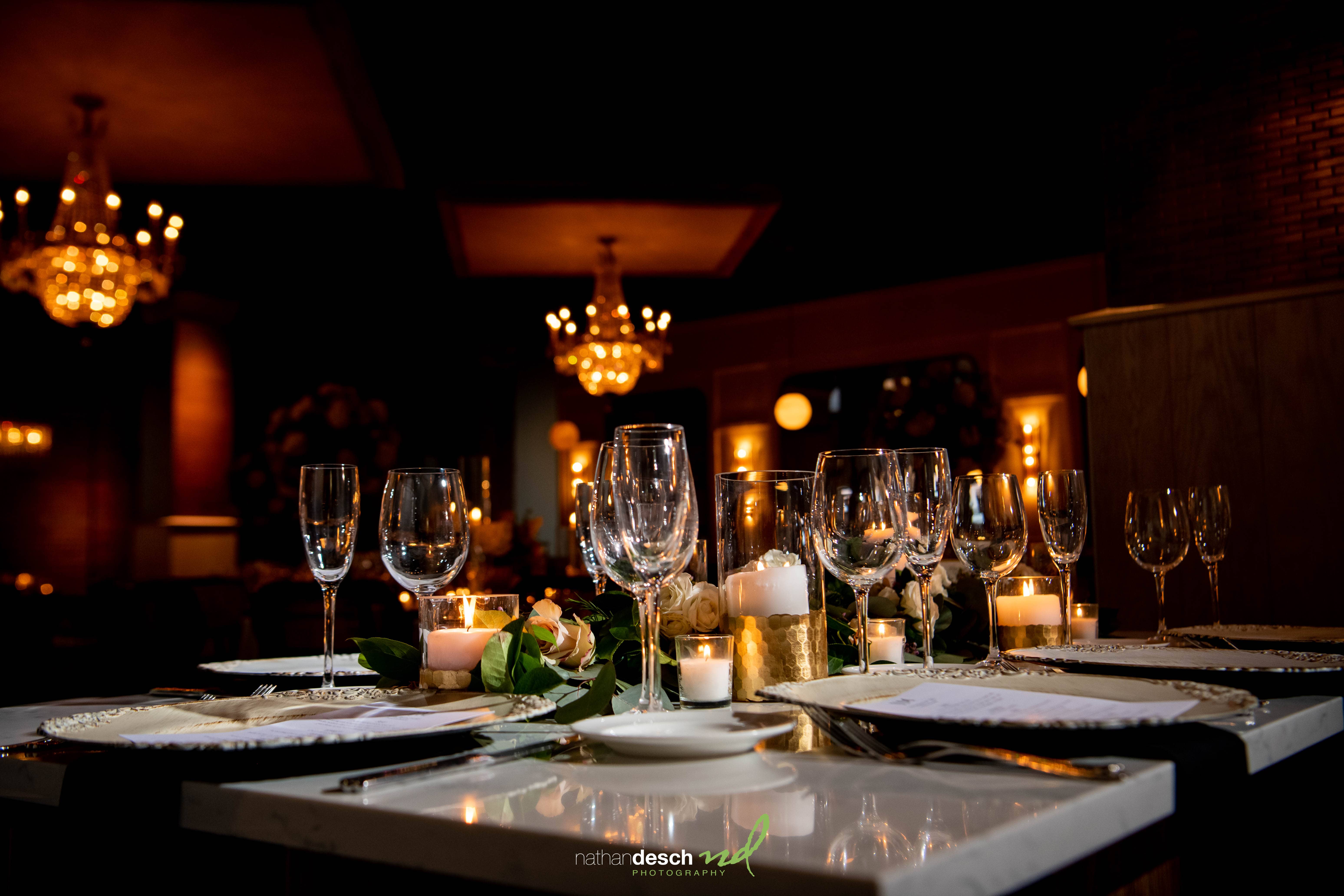 Elegant spring wedding reception table at Tendenza with candles, wine glasses, floral decor, and glowing chandeliers.