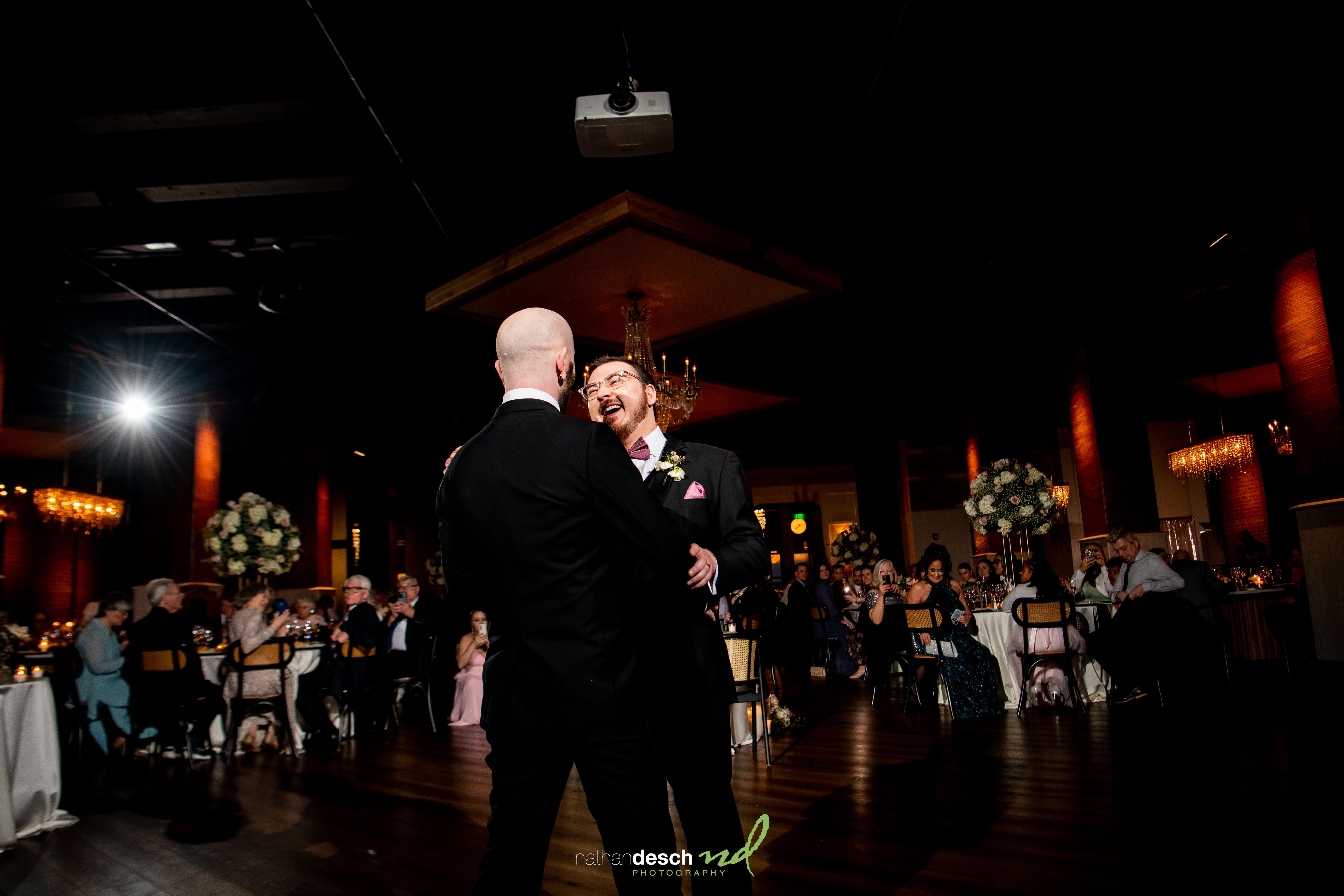 Two grooms share a joyful first dance at Tendenza wedding, surrounded by celebrating guests and elegant spring decor.
