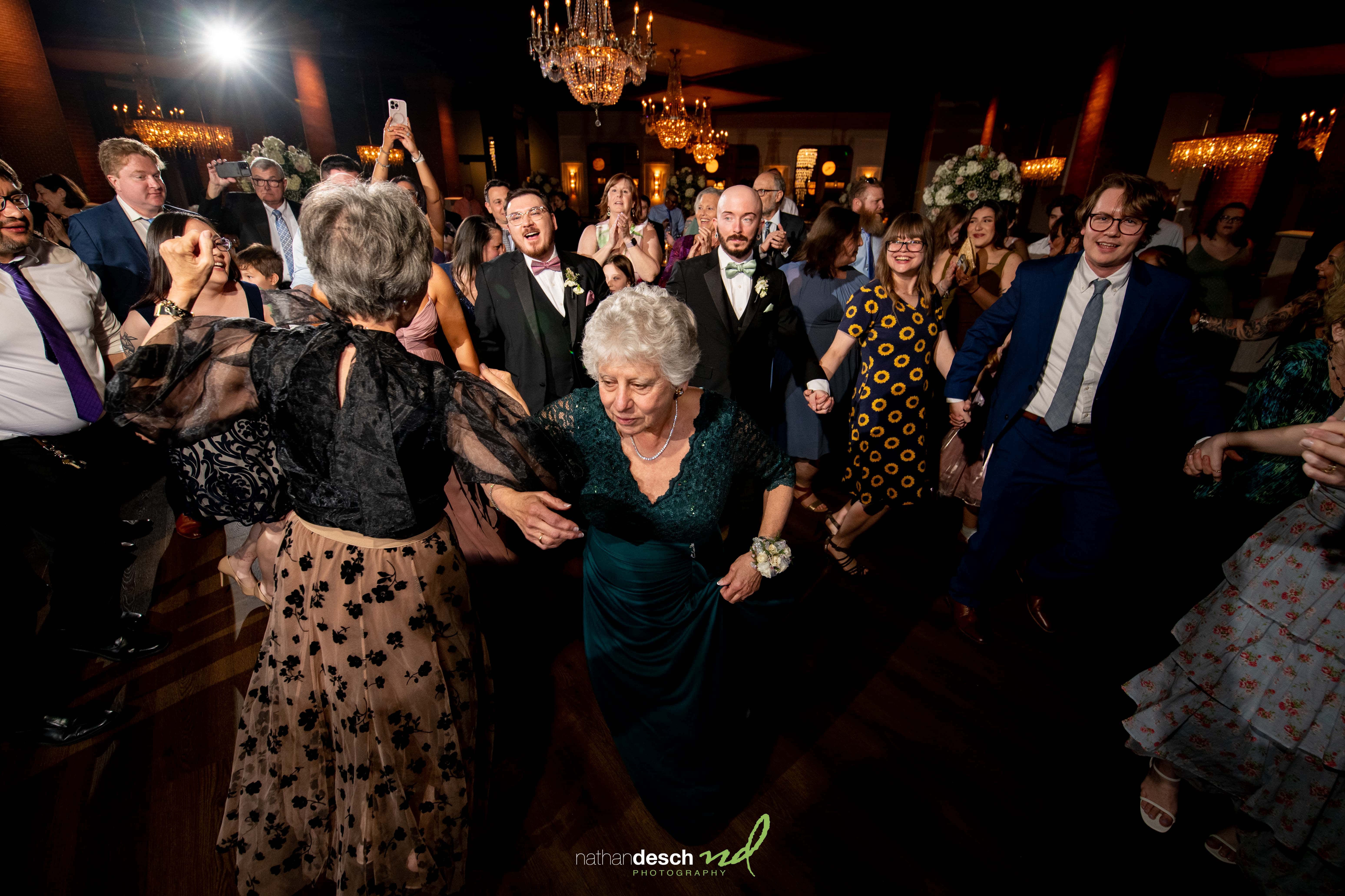 Joyful spring wedding at Tendenza with guests of all ages dancing, led by a smiling elderly woman in a green dress.
