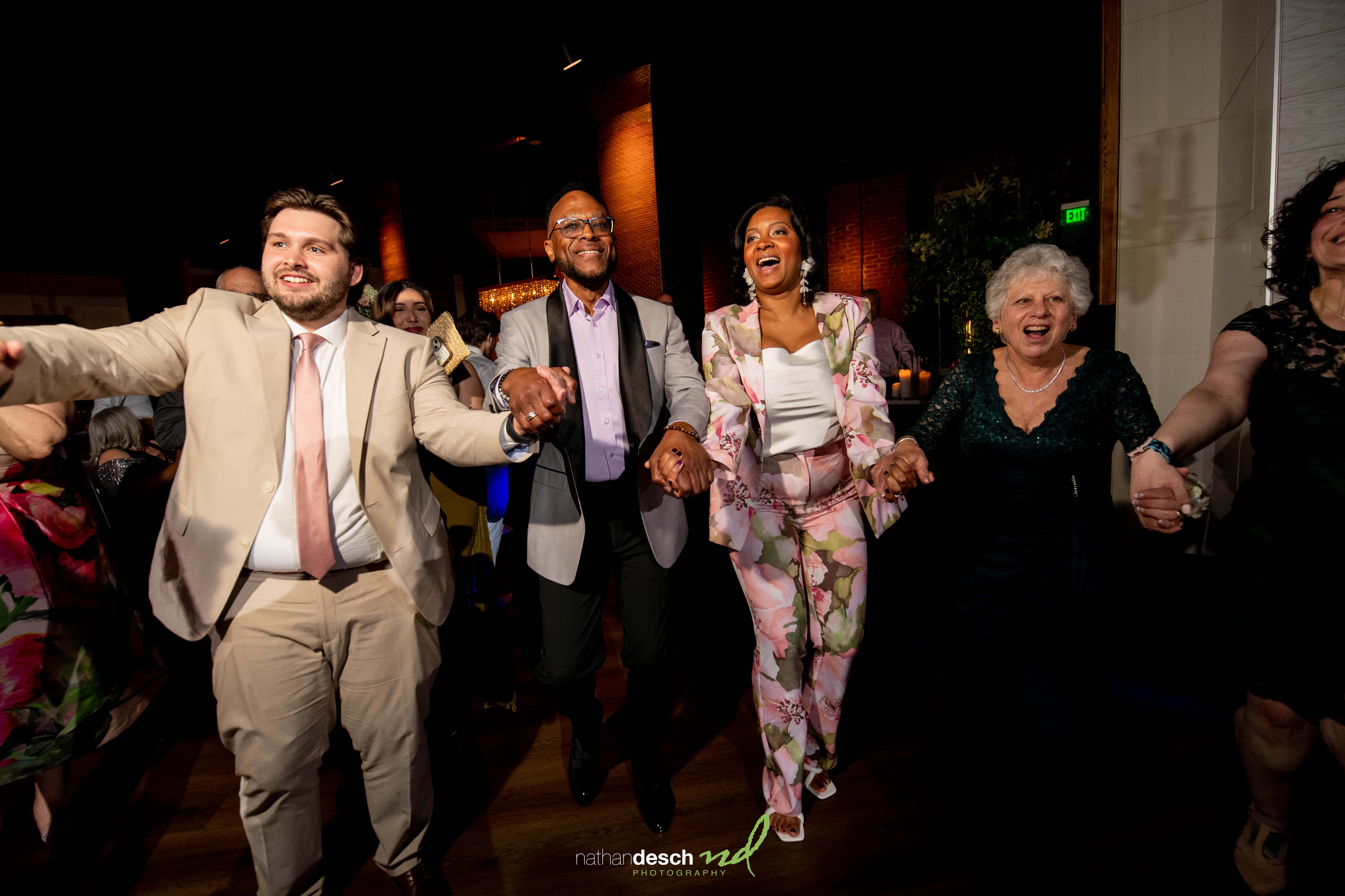 Joyful wedding guests in formal attire dancing and smiling under bright lights at Tendenza spring wedding reception.
