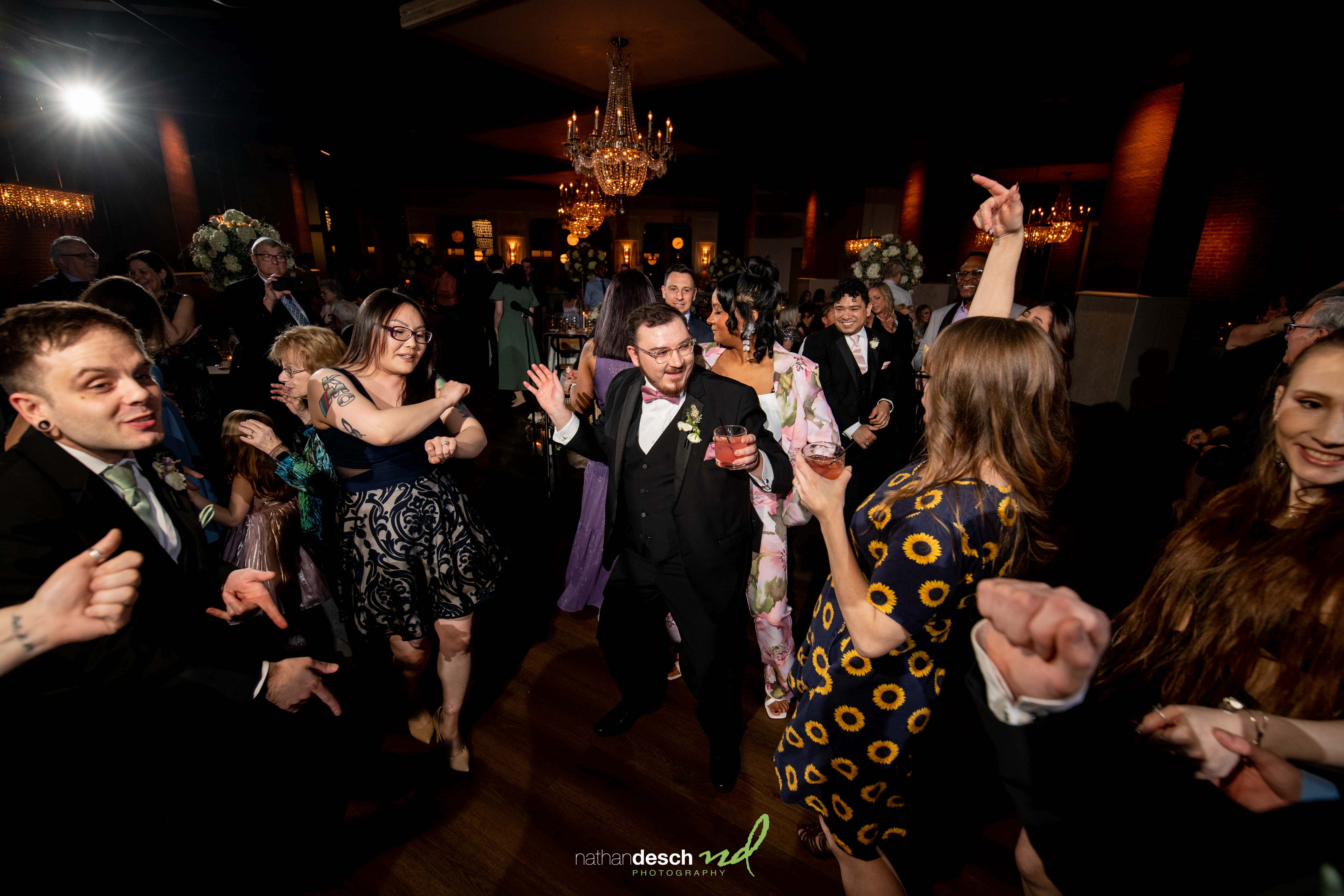 Guests in elegant attire dance joyfully at a spring wedding reception at Tendenza, smiling under warm event lighting.