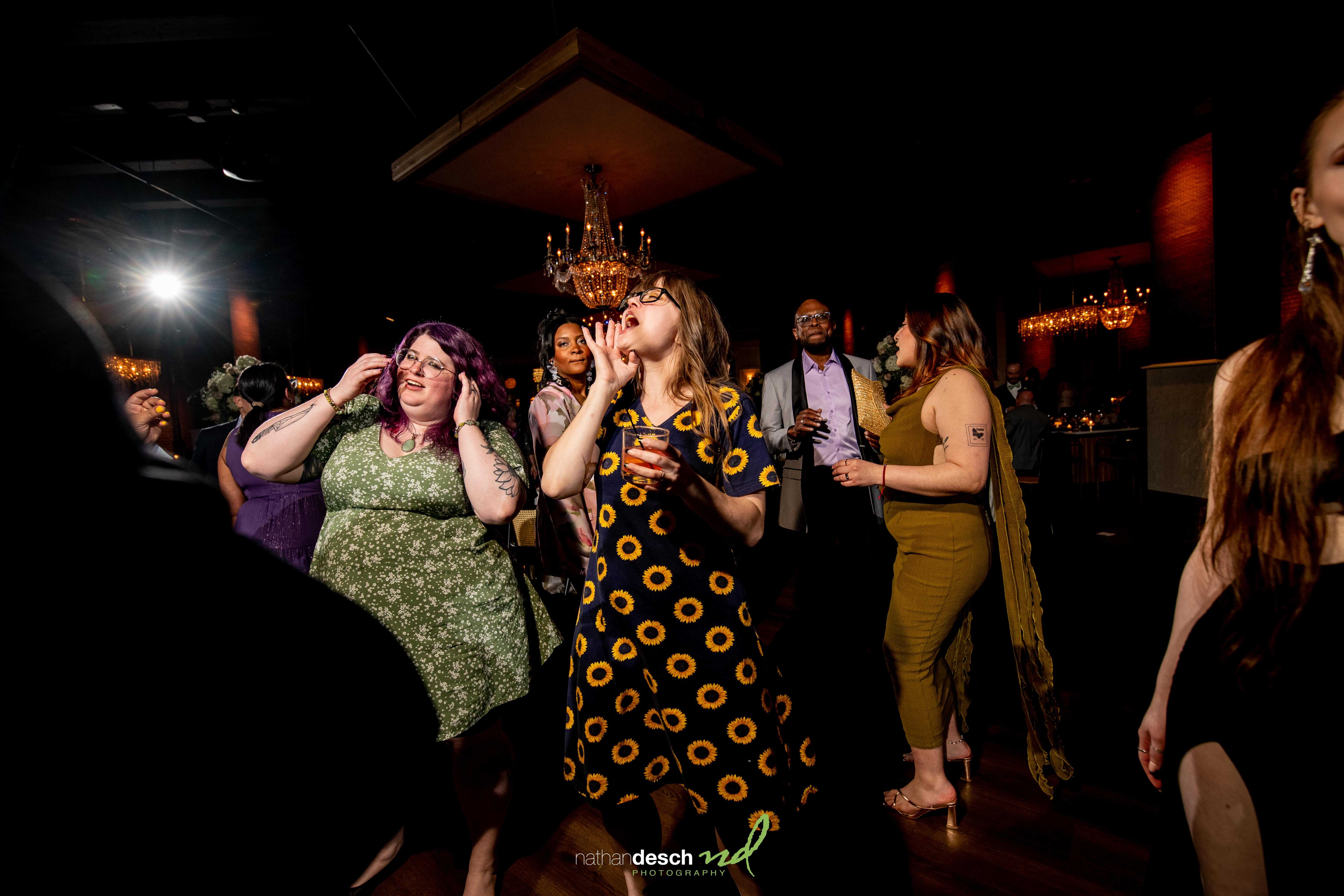 Guests dancing and celebrating at a vibrant spring wedding reception at Tendenza with chandeliers and colorful outfits.