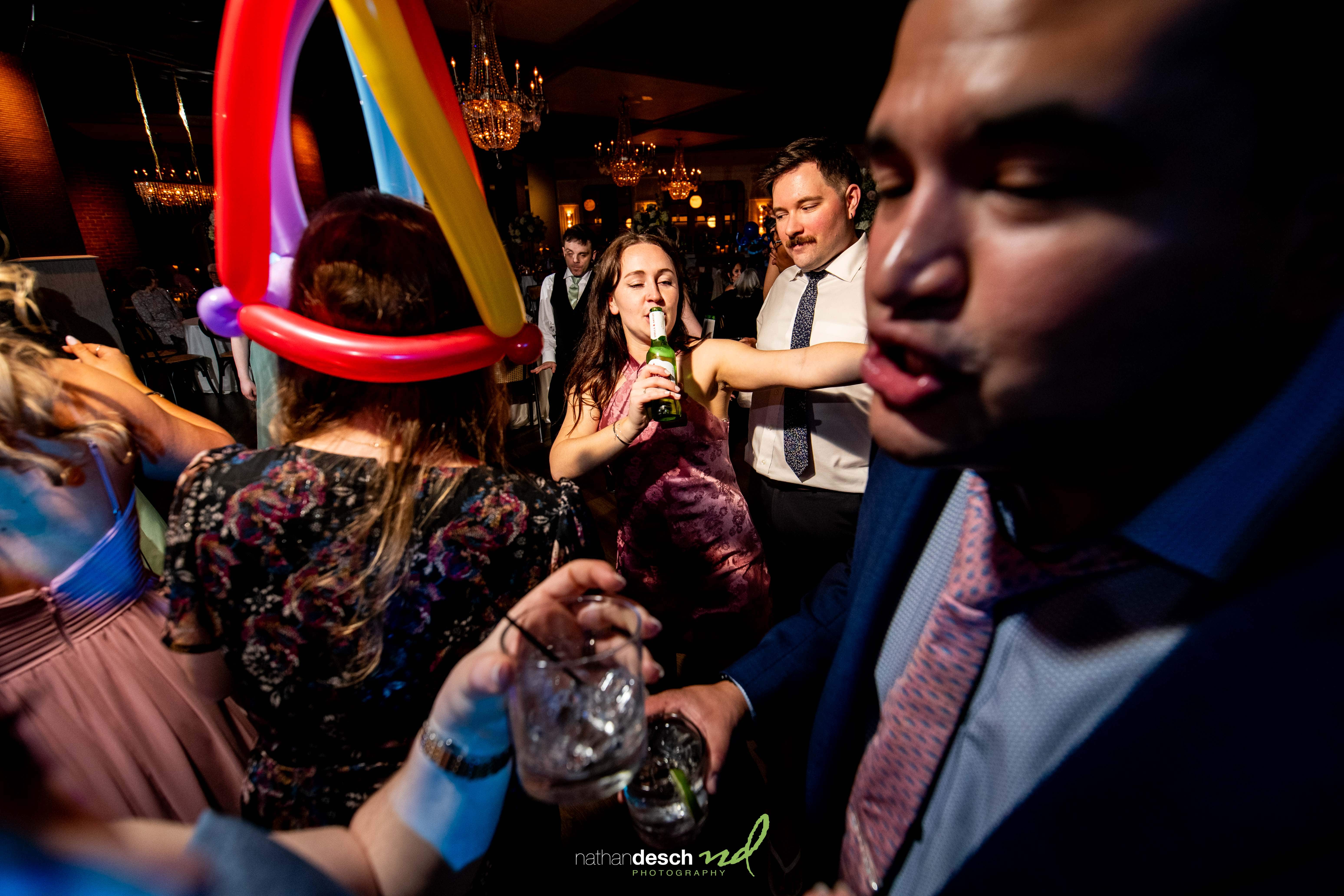 Guests dancing and celebrating at a lively spring wedding reception at Tendenza, with balloon hats and festive drinks.