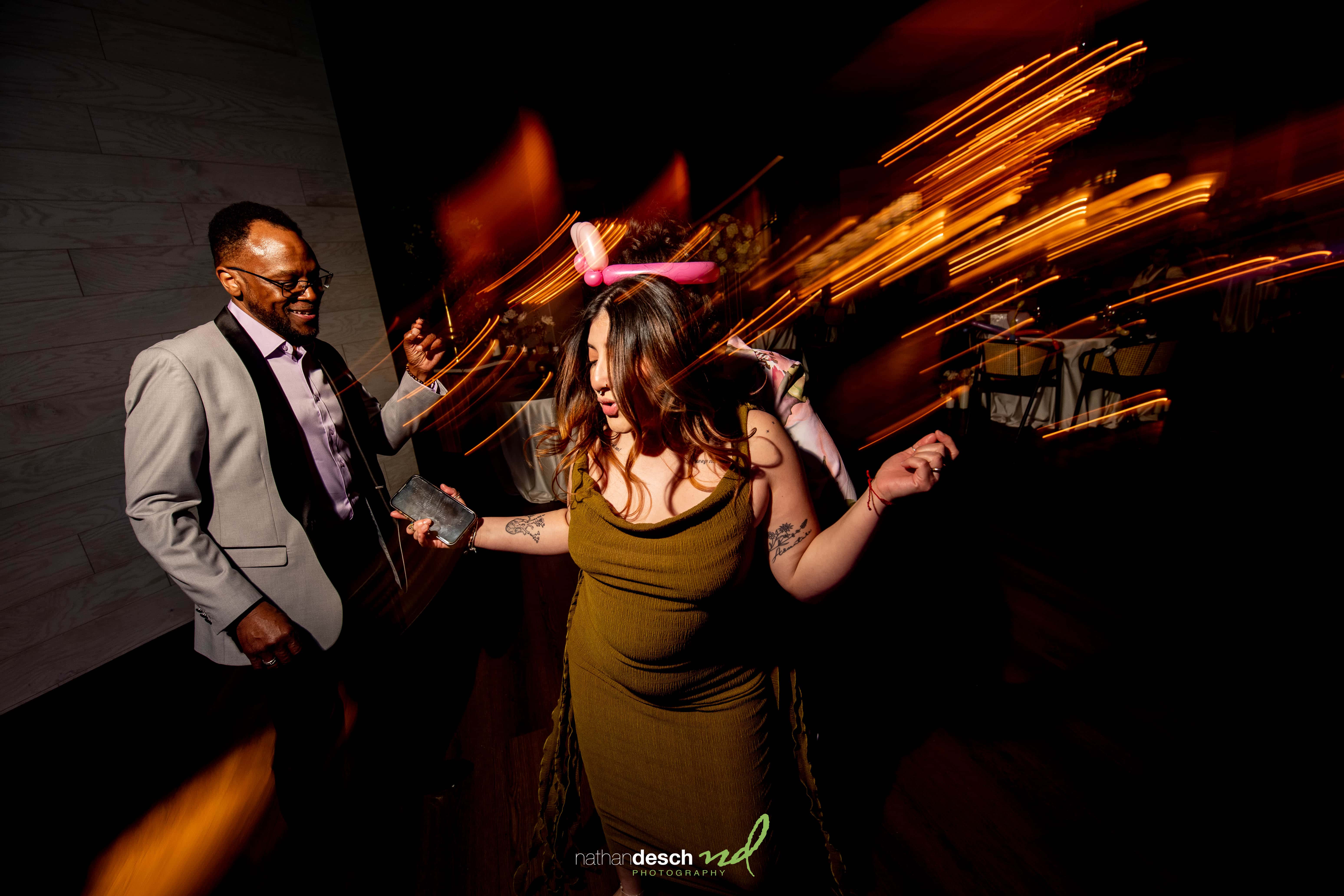 Couple dancing at Tendenza spring wedding; woman in green dress with pink balloon hat, lively lights and joyful atmosphere.