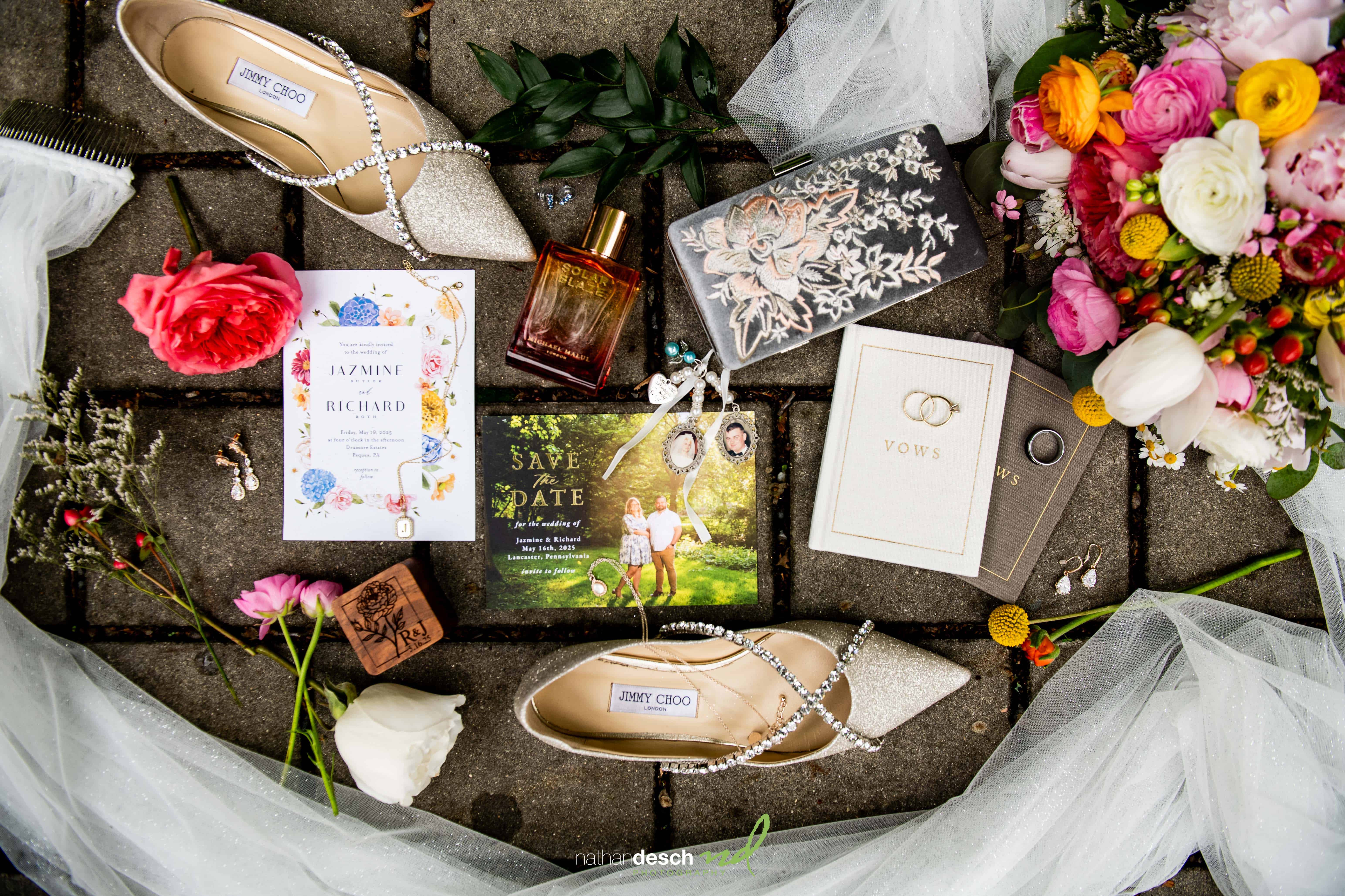 Flat lay of wedding accessories—heels, bouquet, vow book, invites & jewelry—on stone with tulle at Drumore Estate.