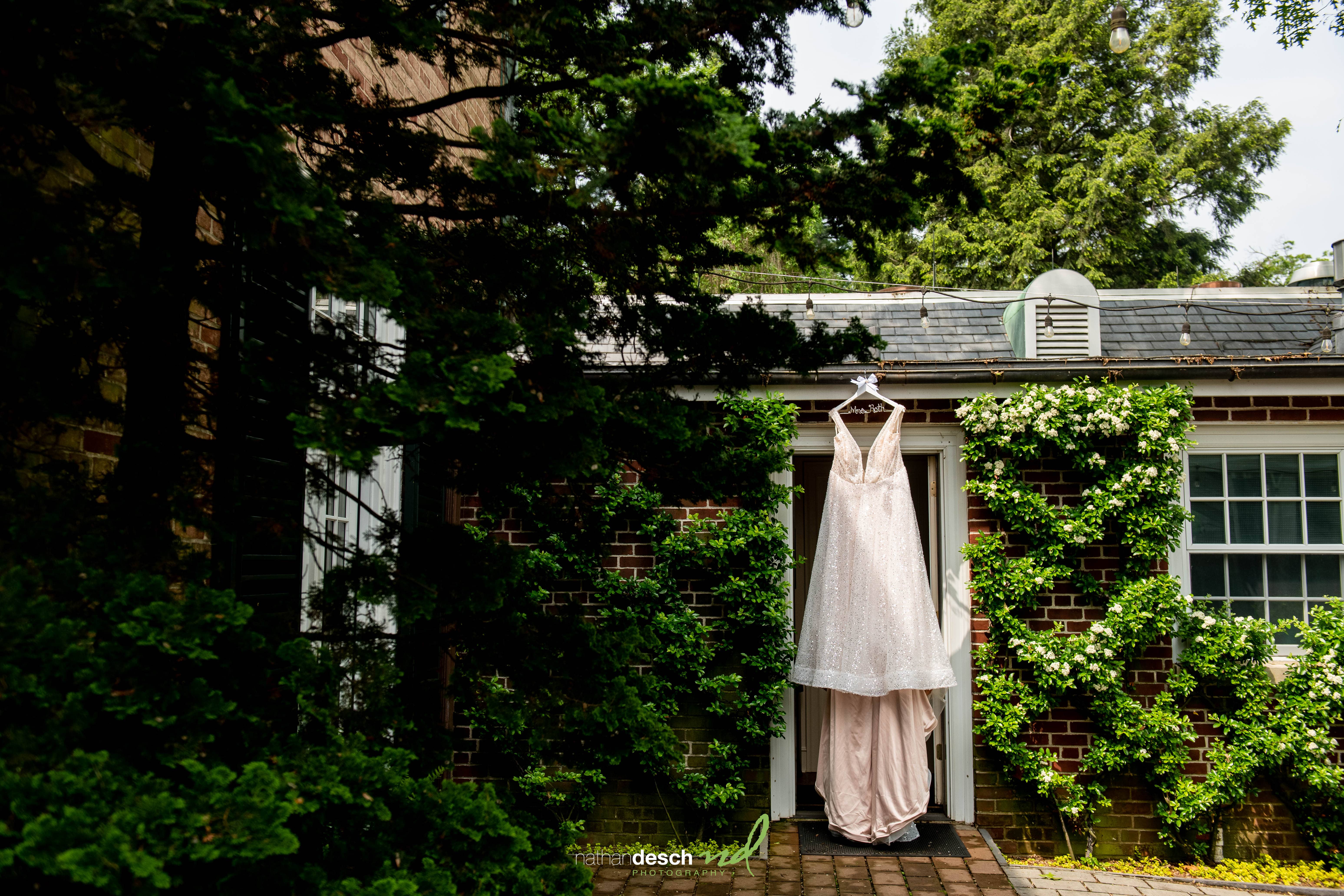 White wedding dress hanging on door at Drumore Estate, surrounded by green vines and sunlight for a spring wedding.