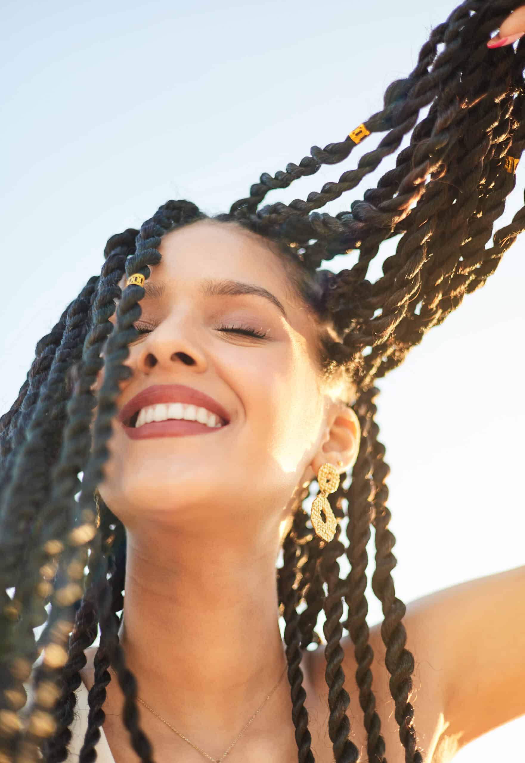 View from below of a cheerful latin american woman with braided hair. Close-up portrait of a young woman of Latin origin with braids in her hair. She is relaxed and smiling with her eyes closed. Sunset light