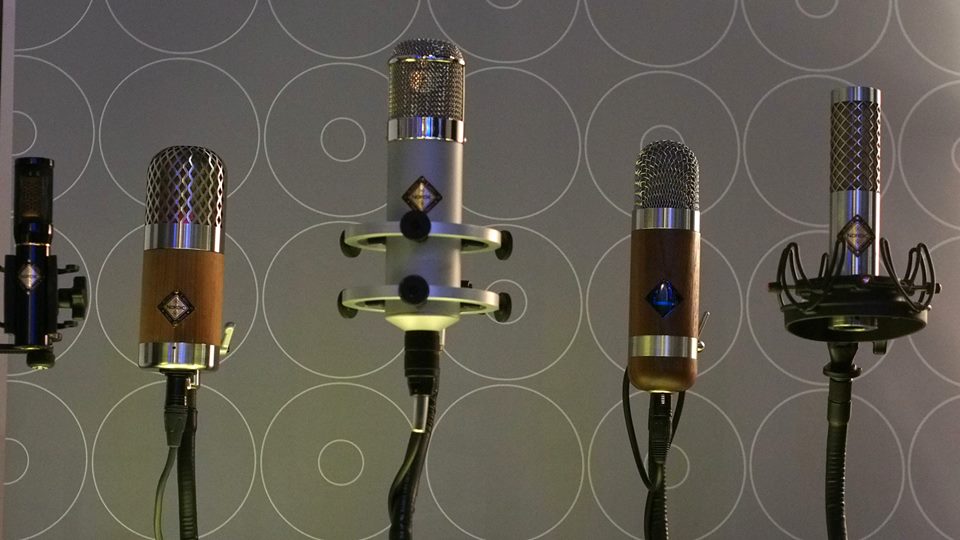 Five Nordic Audio Labs microphones on display in a row against a modern circular-pattern background