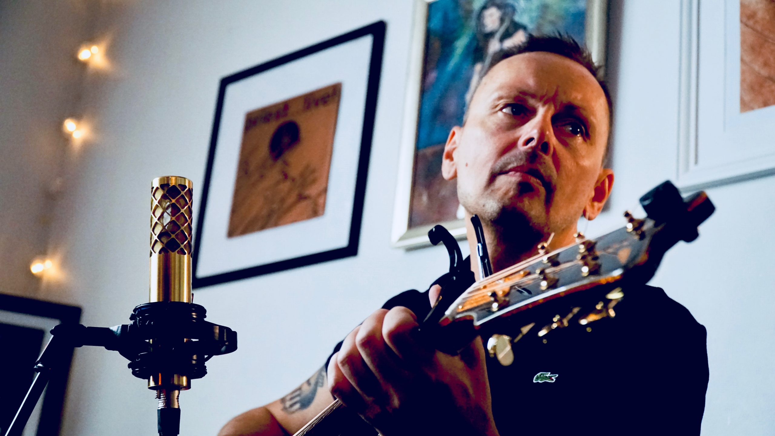 Patrik Linman playing acoustic guitar in a cozy studio with a gold NU-100K microphone in front of him