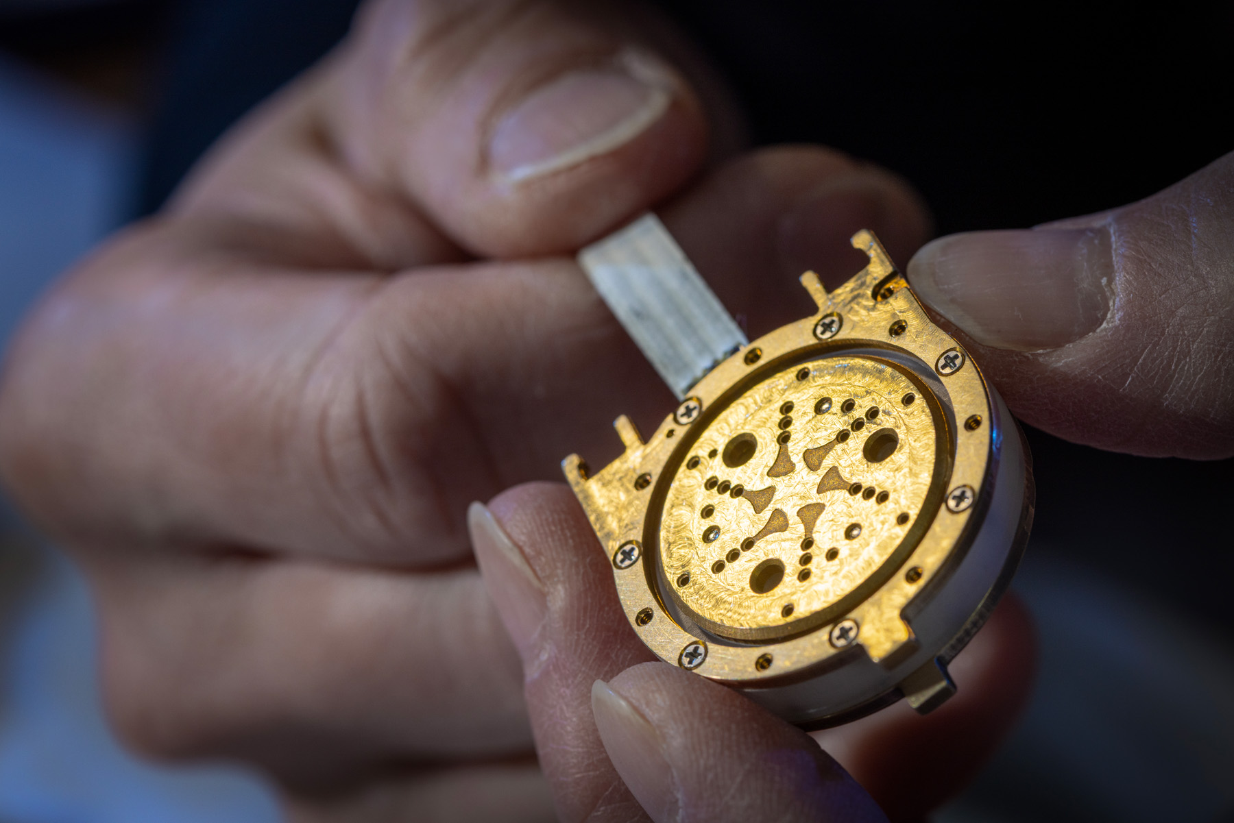 Hands holding a precision-crafted gold microphone capsule during assembly