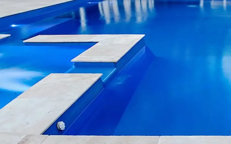 Close-up view of a swimming pool with bright blue water, featuring angular, light-colored tiled edges and underwater steps—perfect inspiration for fiberglass pools or concrete swimming pools in your next pool project.