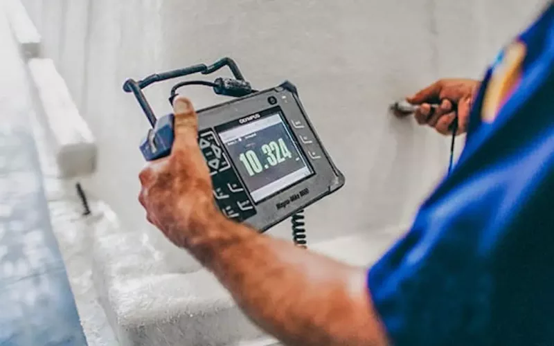 A person in a blue shirt uses an ultrasonic thickness gauge to measure the layer of a white material, often essential during swimming pool installation; the digital screen displays a reading of 10.324.