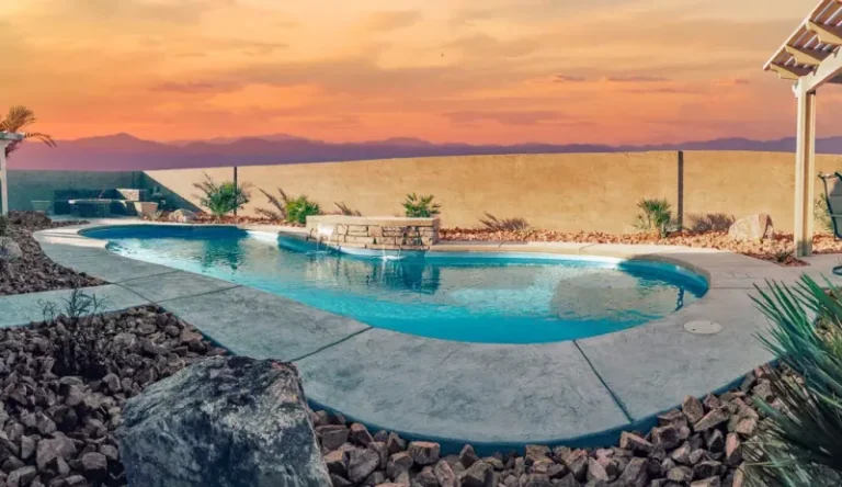 A backyard pool with a cascading waterfall and LED lights at night.