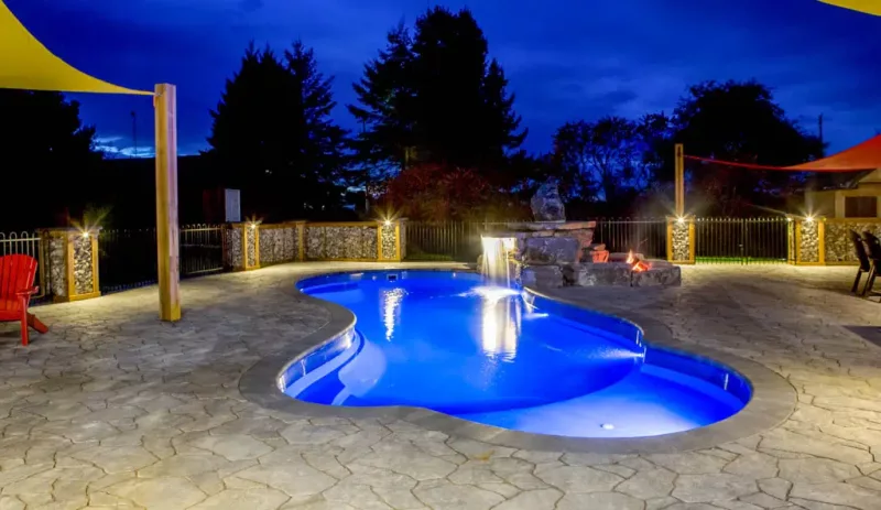Custom swimming pool with waterfall and LED pool lighting at night.