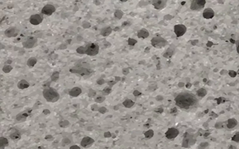Close-up image of a gray, porous surface with variously sized holes and dark spots, resembling pumice stone or aerated concrete—textures often inspected by a swimming pool contractor during swimming pool installation or when working with fiberglass pools.