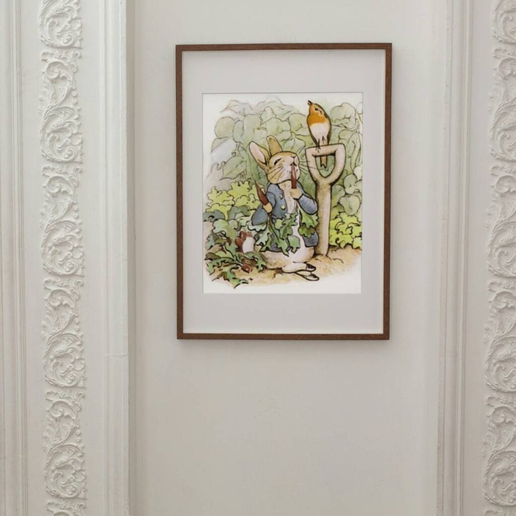 Peter Rabbit munching on radishes in Mr McGregor's garden art print hanging on a white wall.
