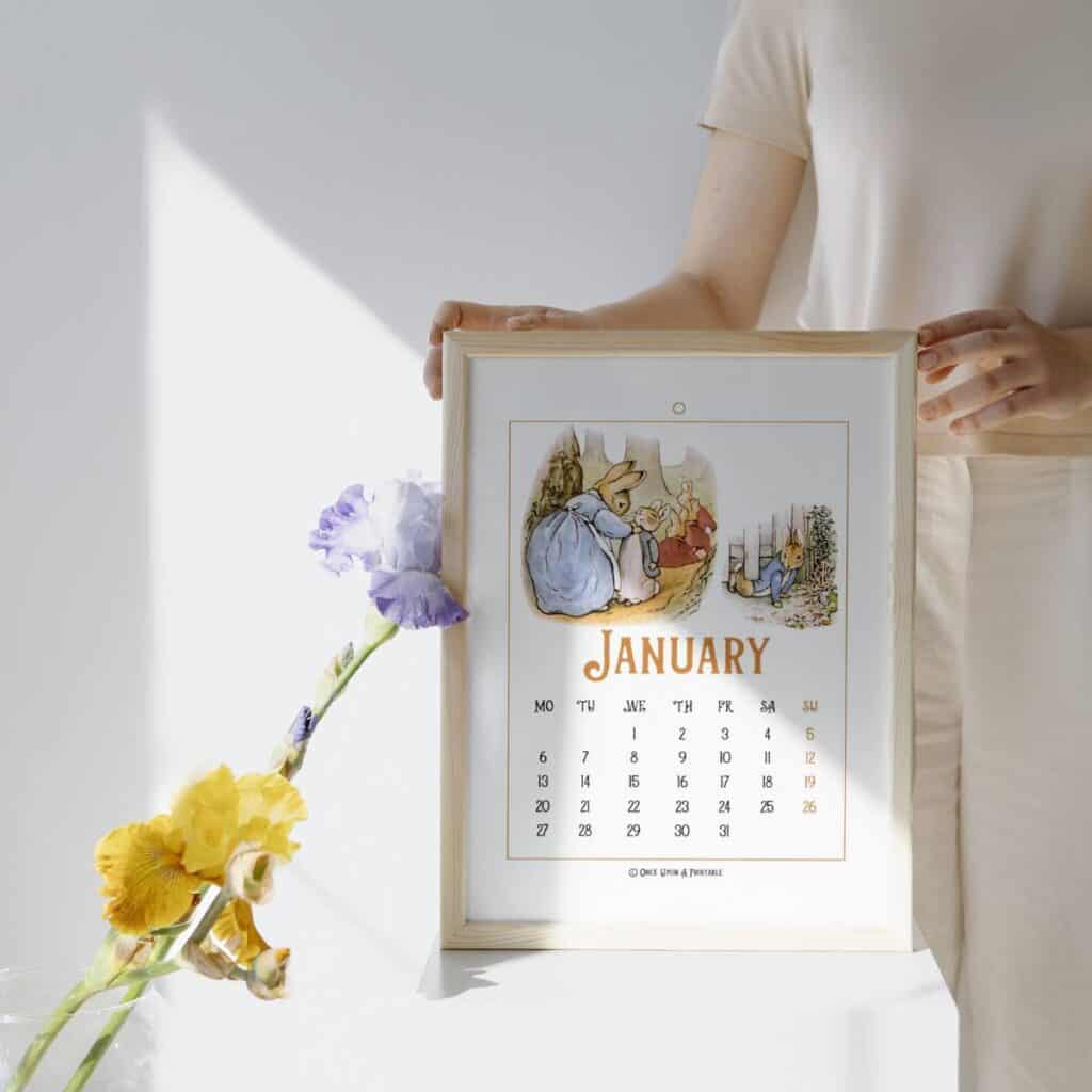 Peter Rabbit illustrated January calendar in a frame with a woman holding it next to Iris's in a vase.