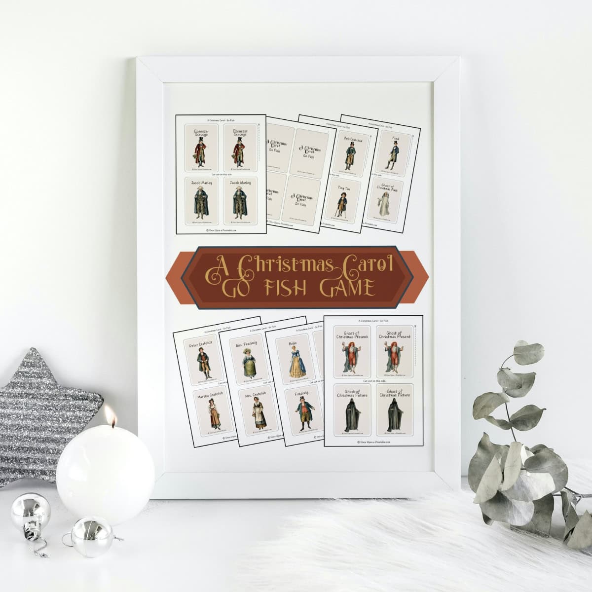 A Christmas Carol Go Fish Game cover page framed and sitting next to a few ornaments and a sprig of eucalyptus.