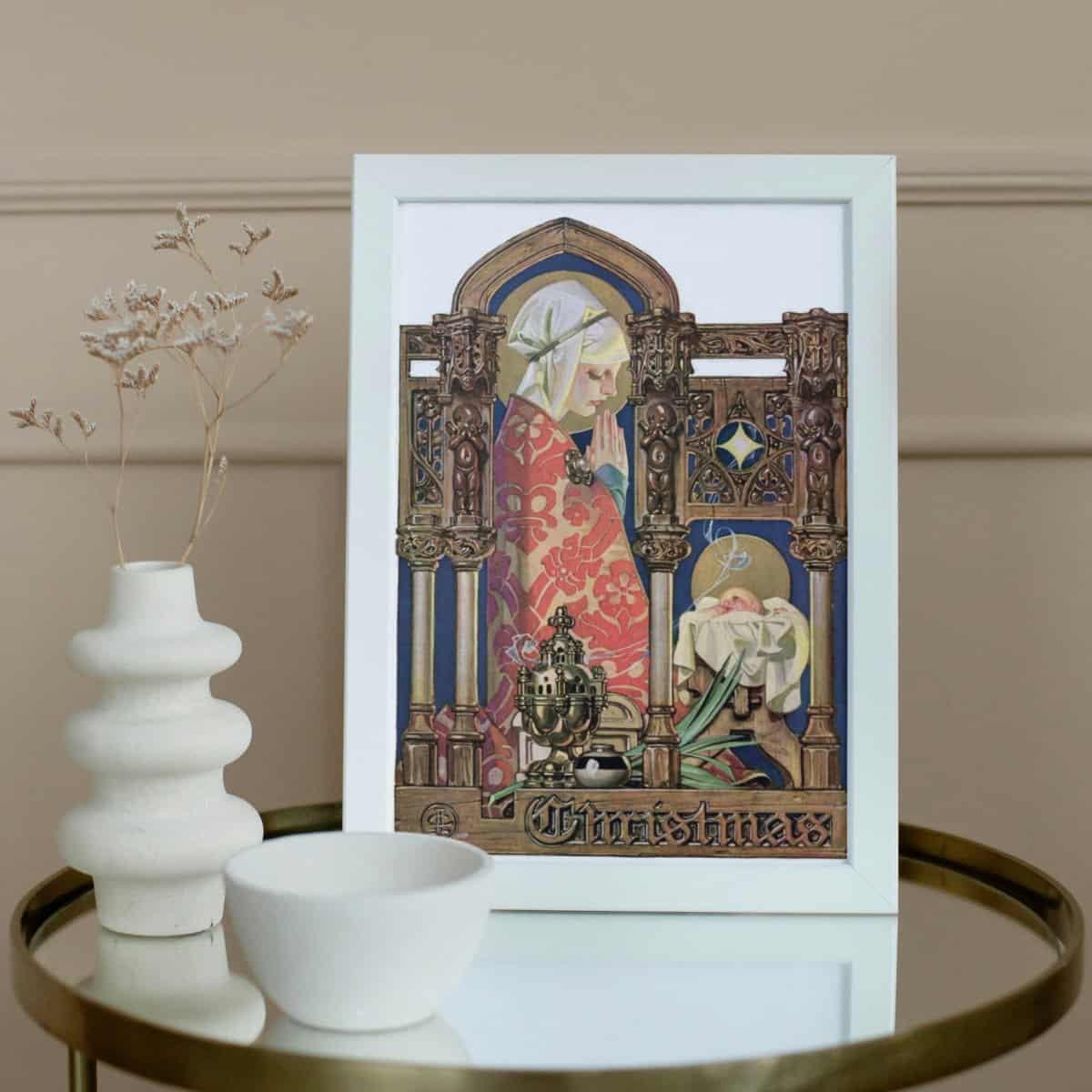 a vintage illustration of Mary and baby Jesus in a basket framed and displayed on a glass table with two white vases.