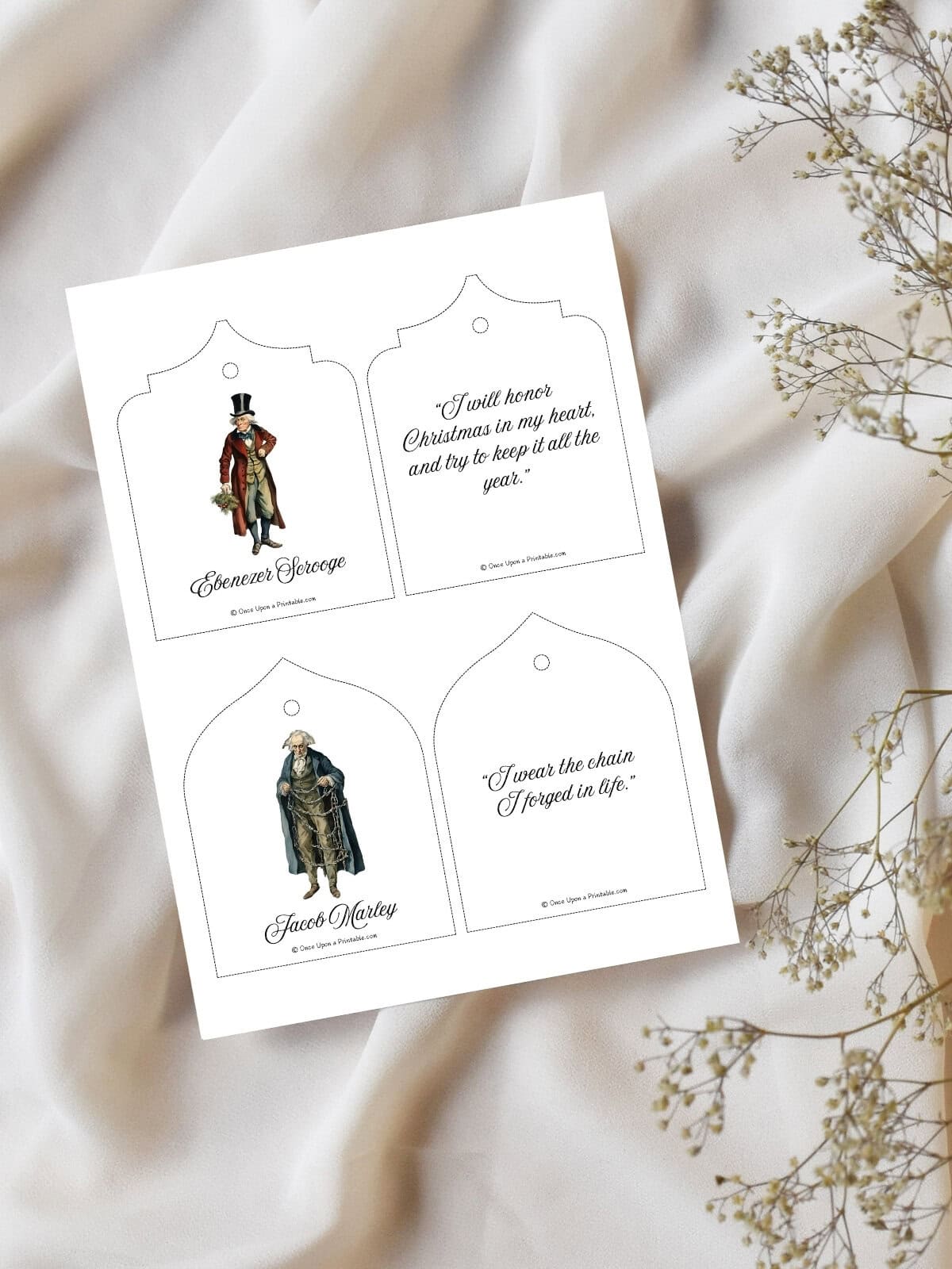 Scrooge and Marley printable christmas tree oranments page laying on a white table cloth with baby's breath.