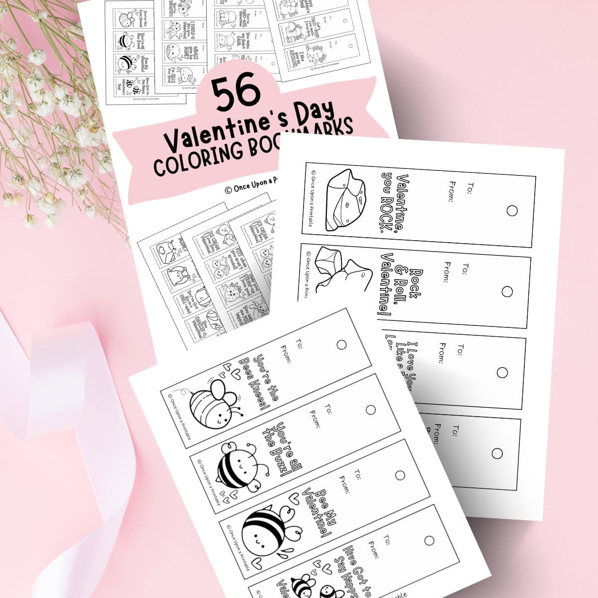 Kid's coloring bookmarks for Valentine's Day laying on a pink background with ribbons and baby's breath flowers.