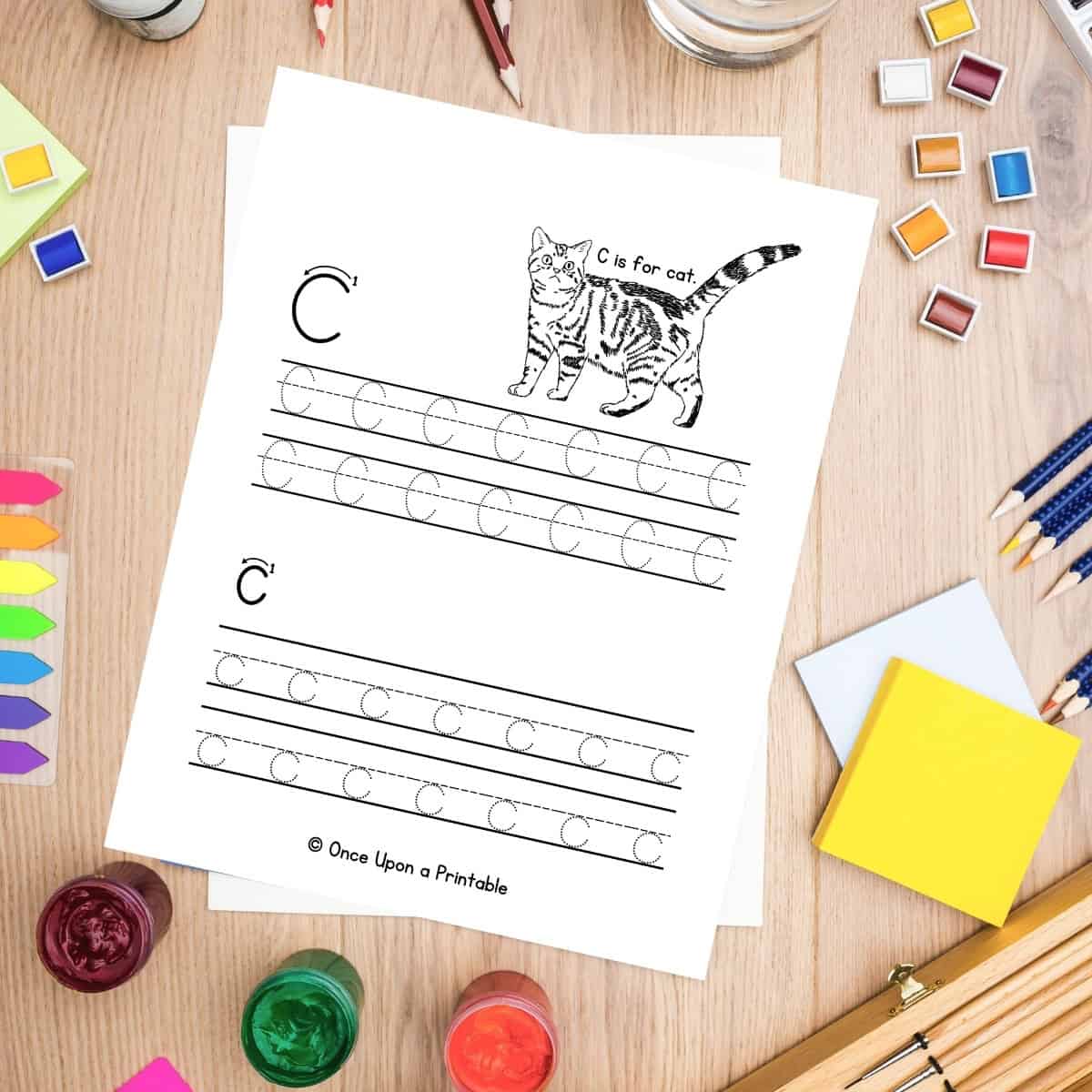 Letter C and lowercase c letter practice worksheet laying on a wooden table with coloring supplies.