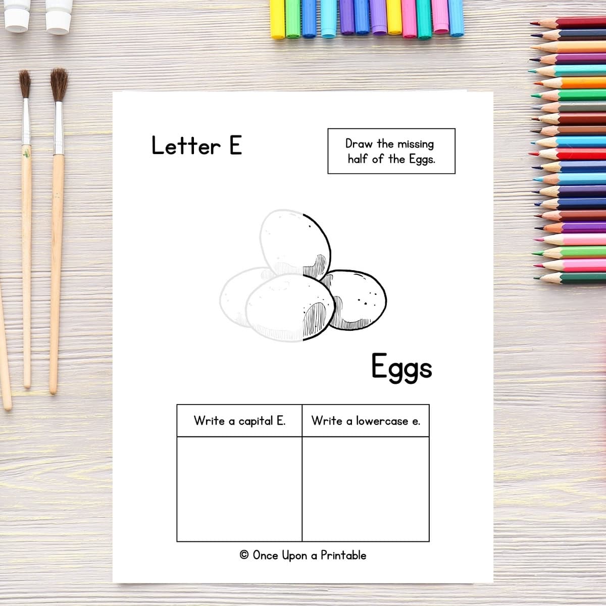 Finish the eggs drawing and letter practice page laying on a table with coloring pencils and paint brushes.