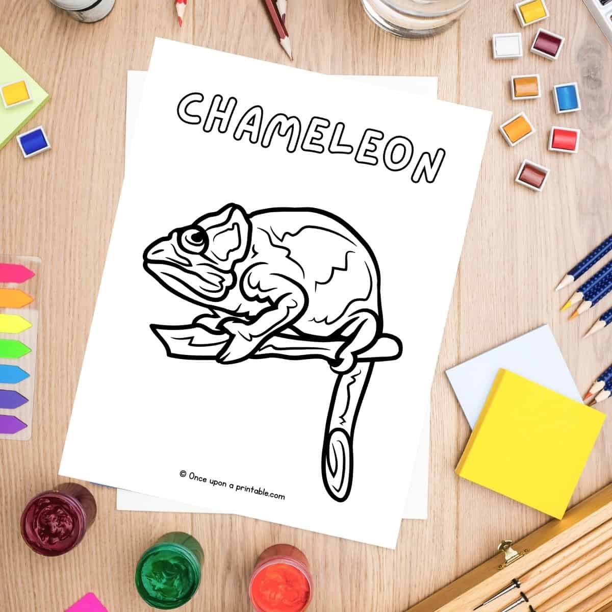 C is for Chameleon coloring page laying on a wooden table with art supplies.