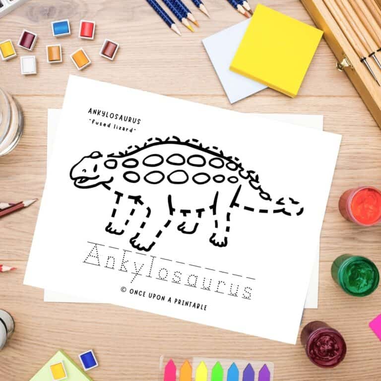 Ankylosaurus tracing and coloring page laying on a table with coloring supplies.