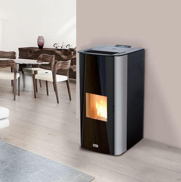 Een CV Moederhaard Tepor Steel hydro DD 14-32kW pelletkachel met glazen deur verbetert een minimalistische woonkamer. Zichtbare vlammen binnenin creëren sfeer. In de buurt staan een houten eettafel en stoelen tegen een neutrale muur, met een lichtgekleurd tapijt dat de houten vloer gedeeltelijk bedekt.