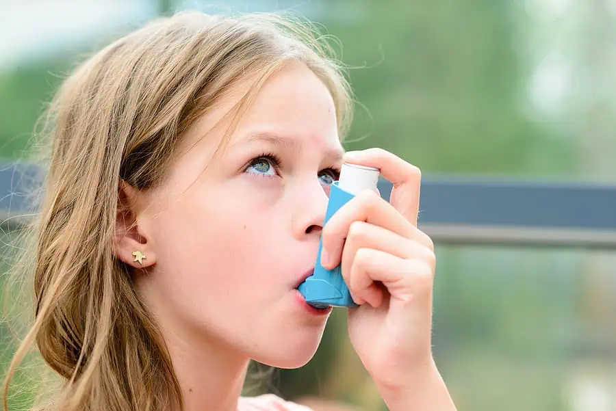 Girl using a blue inhaler outdoors.