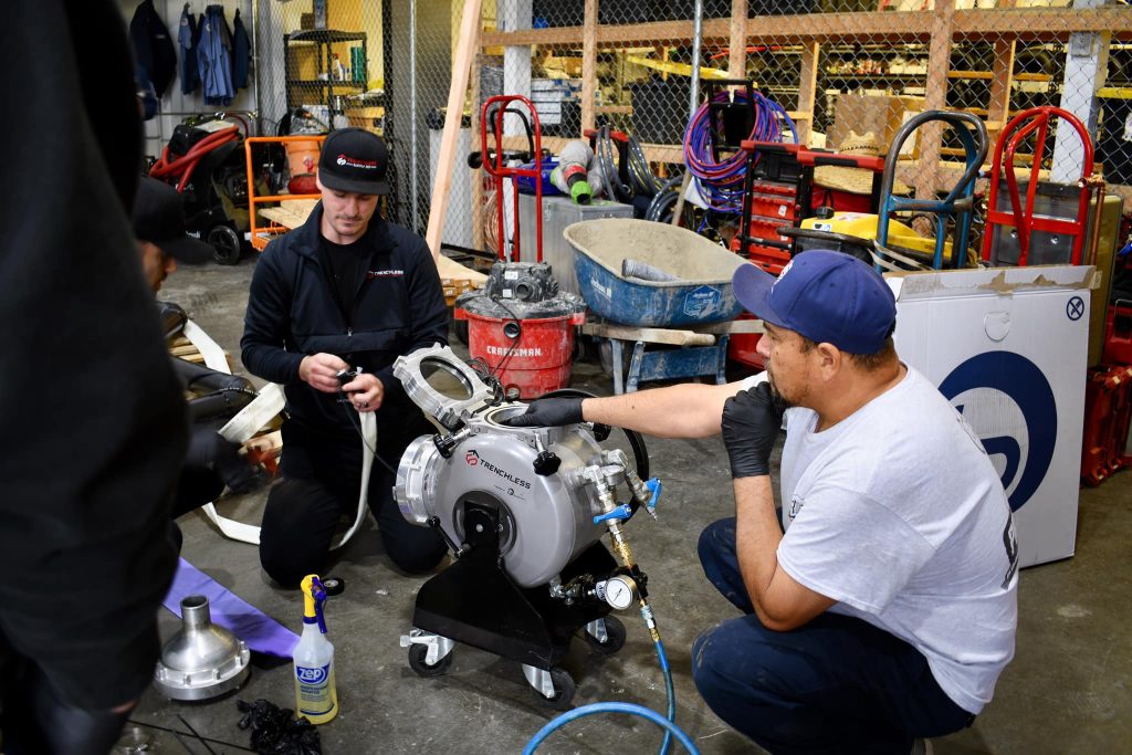 Two workers at Prodigy Sewer and Drain fix a big machine, showing their plumbing skills and teamwork in Smyrna, TN.