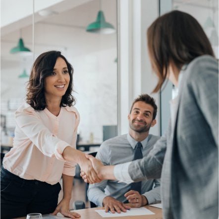 Profesionales en una reunión estrechando manos, simbolizando el éxito en la selección de talento. Representa la identificación de perfiles cualificados y la creación del match perfecto entre empresas y candidatos.