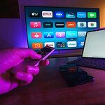 a hand holding a remote control next to a laptop