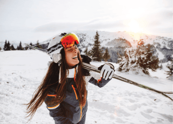A happy woman standing in snowy mountains holding her snow skis