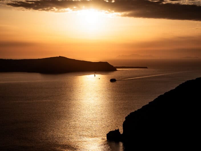 A golden sunset over the Caldera in Santorini. A boat can be seen making it's way back to the port