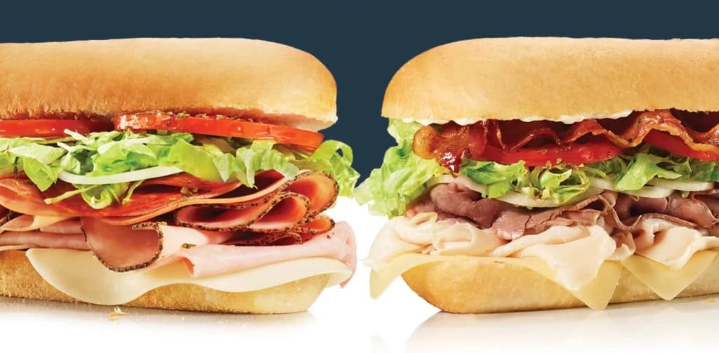 Two sandwiches with meats, lettuce, tomato, cheese.