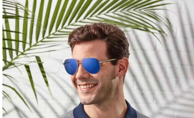 Man smiling with blue sunglasses, palm leaf shadow.