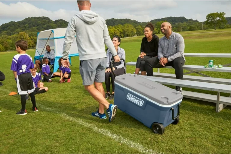 People watching kids play soccer on field bench.