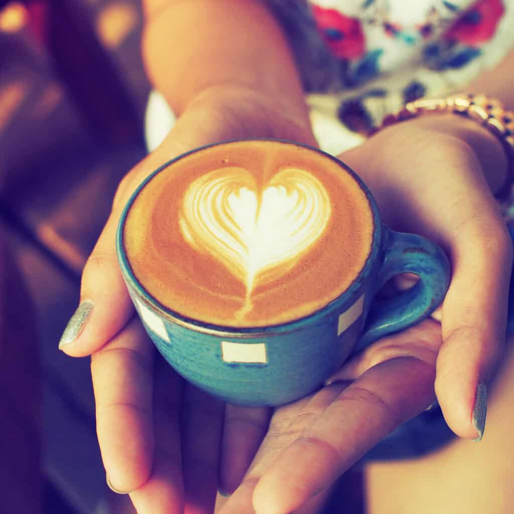 hand and cup of coffee latte art on the wood background vintage